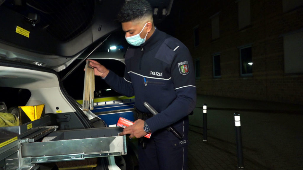 Kommissaranwärter bei der Verkehrskontrolle am Kofferraum eines Polizeiautos.