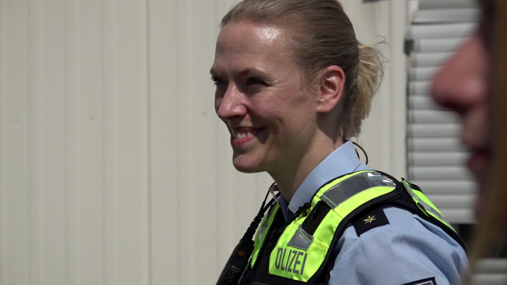 Polizeirätin Vera in blauem Hemd und mit Warnweste, lächelnd.
