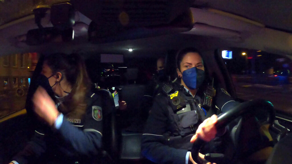 im Polizeiauto mit drei Frauen, die alle Uniform und Maske tragen.